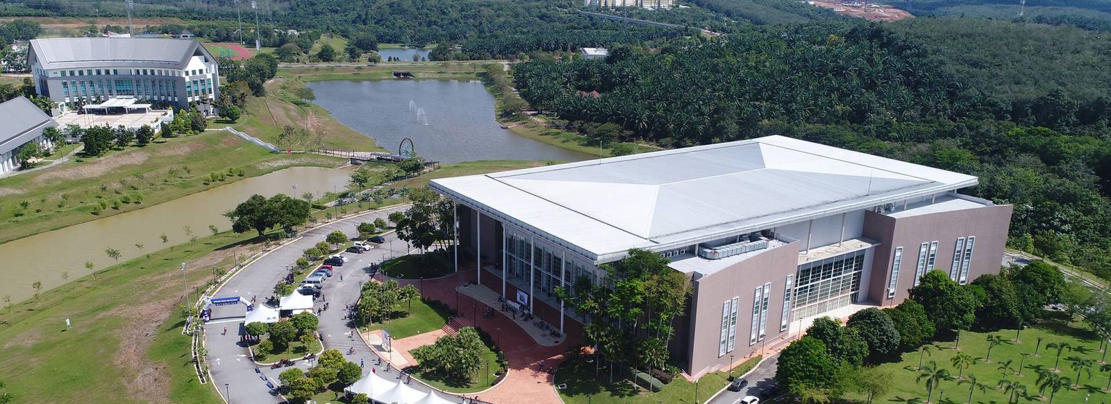 Dewan besar UTeM di tepi tasik dengan pancutan air, dikelilingi kawasan hijau